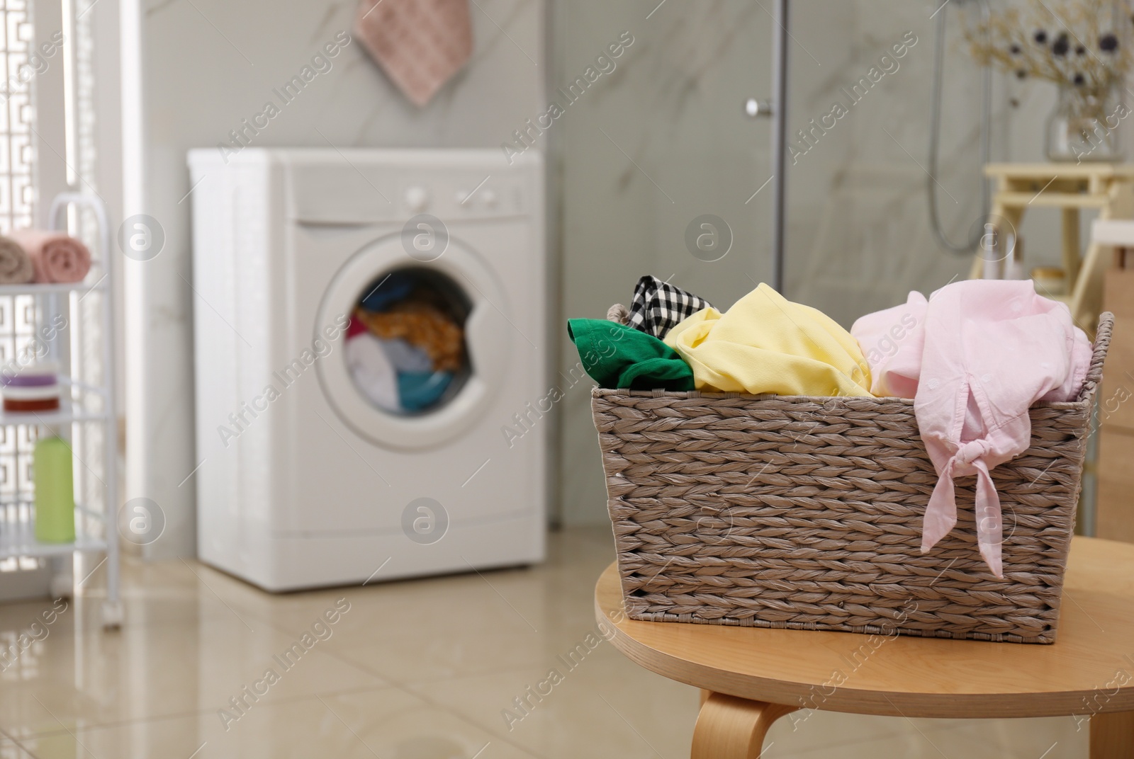 Photo of Wicker laundry basket full of different clothes on table in bathroom