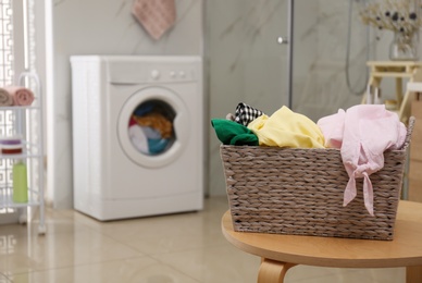 Wicker laundry basket full of different clothes on table in bathroom