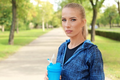 Woman with bottle of protein shake in park. Space for text