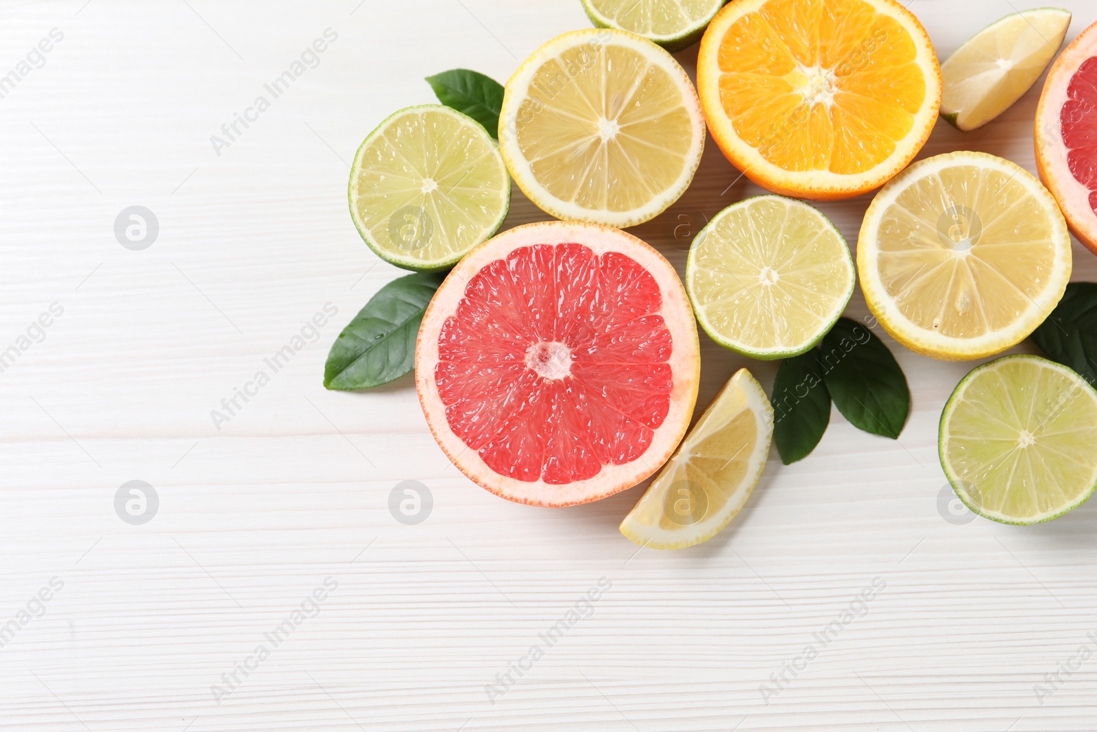 Photo of Different cut citrus fruits and leaves on white wooden table, flat lay. Space for text