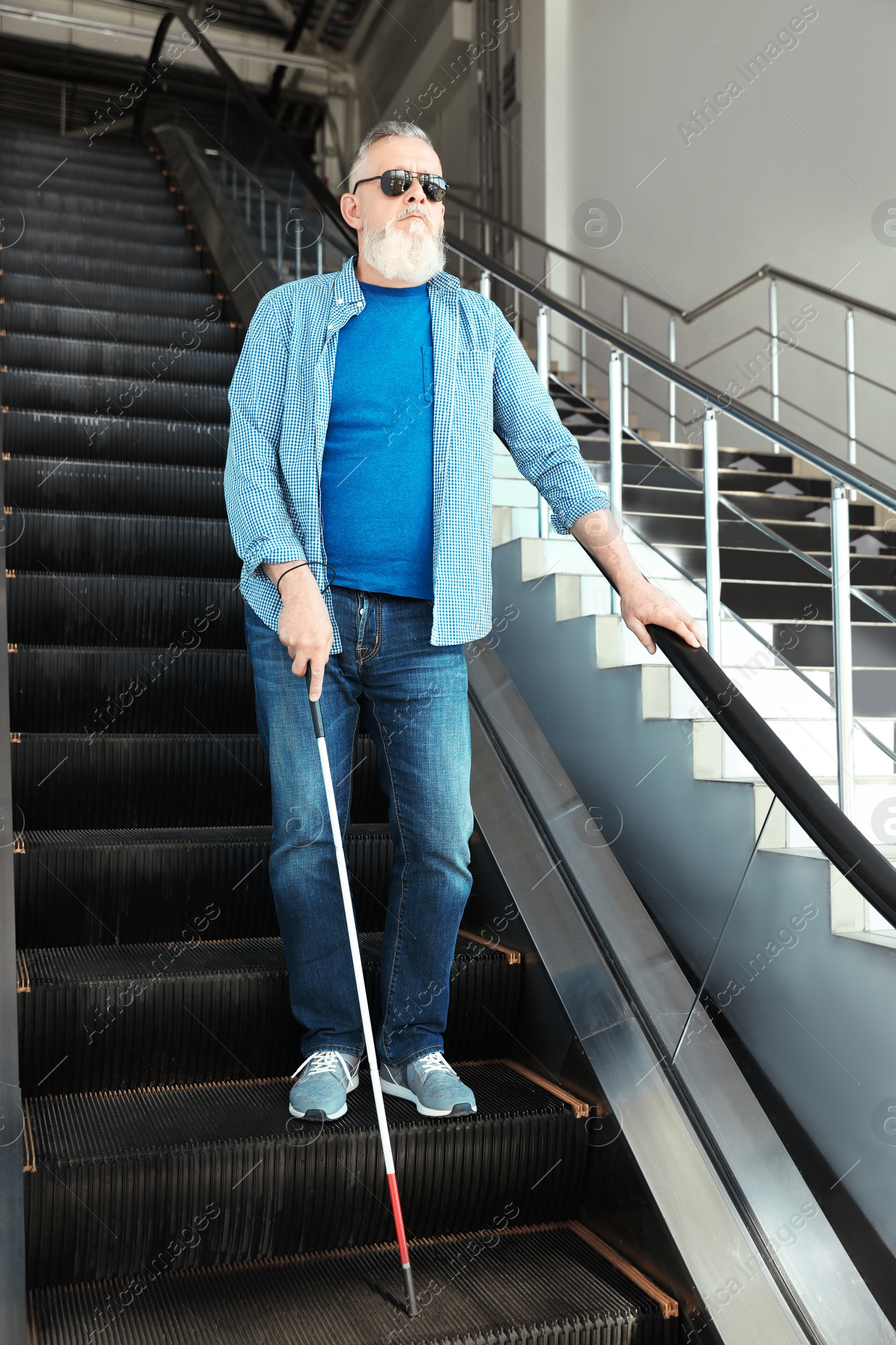 Photo of Blind person with long cane on escalator indoors