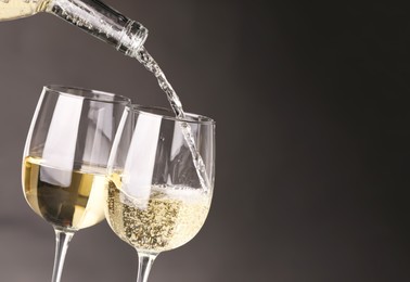 Pouring white wine into glass against grey background, closeup. Space for text