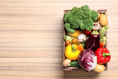 Crate with different fresh vegetables on wooden background, top view. Space for text