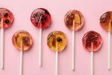 Photo of Sweet colorful lollipops with berries on pink background, flat lay