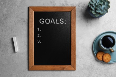 Image of Blackboard with word GOALS and empty checklist on light grey stone background, flat lay