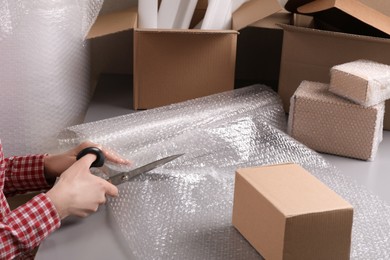 Photo of Woman cutting bubble wrap at table in warehouse, closeup