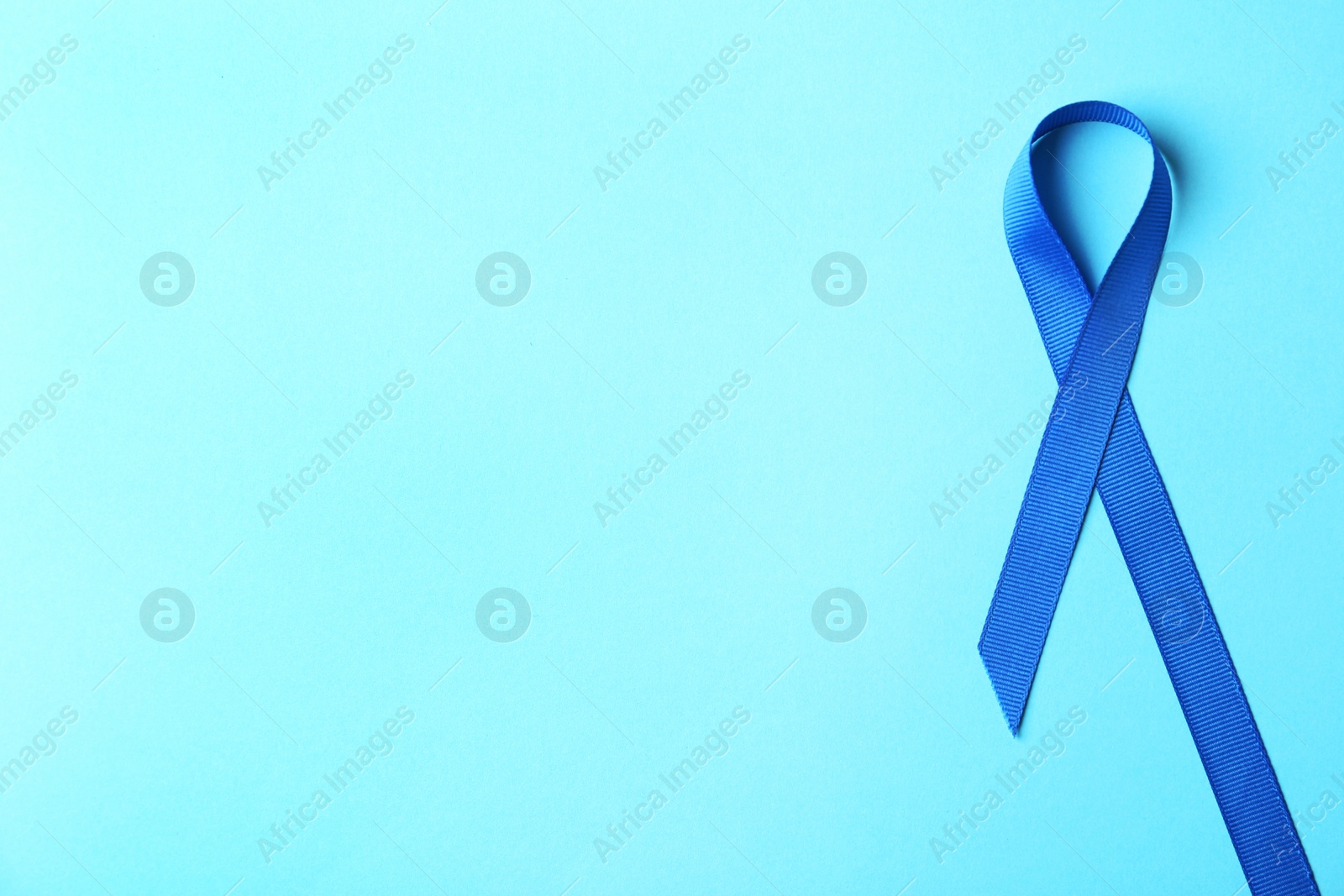 Photo of Blue ribbon on color background, top view with space for text. Colon cancer awareness concept