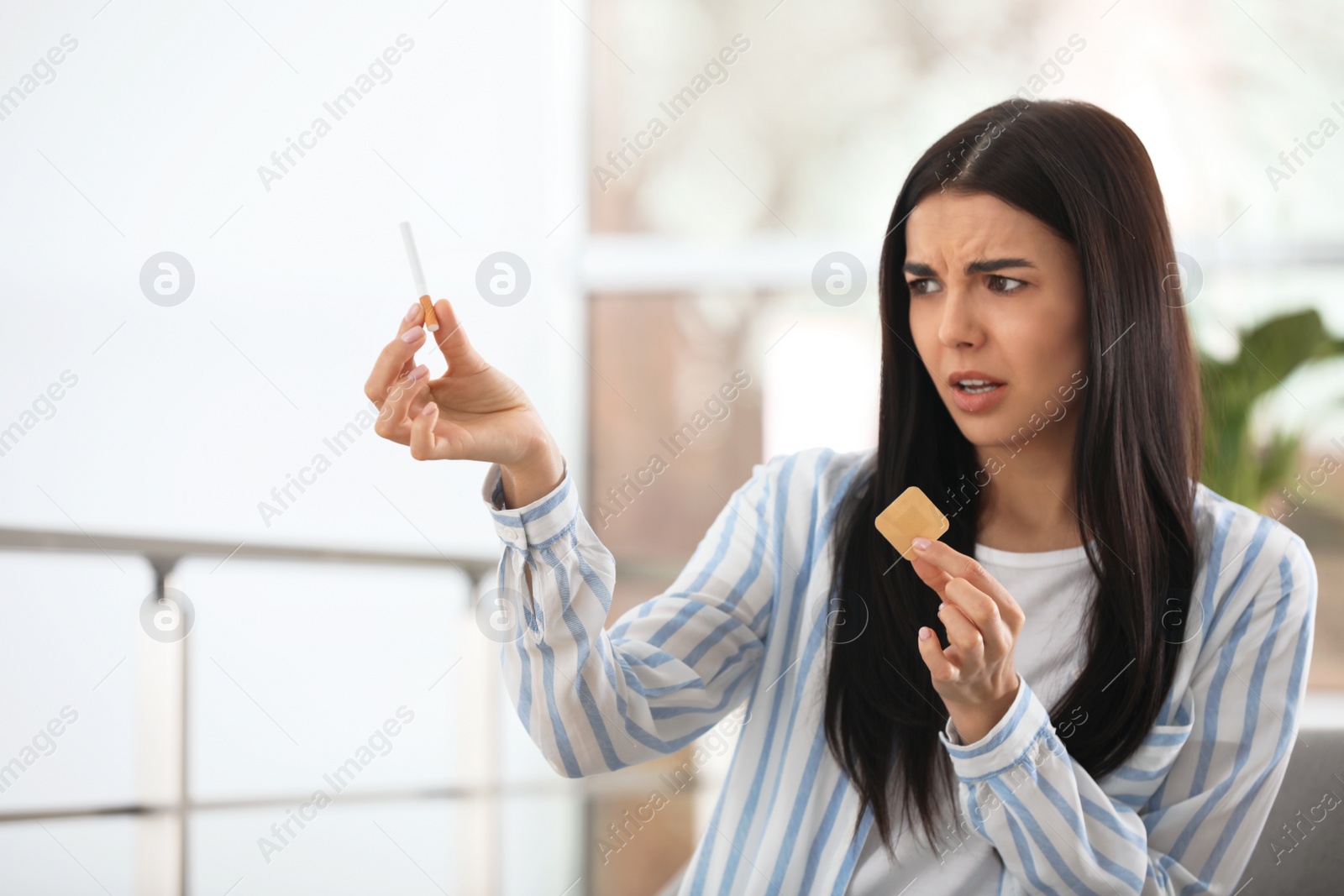 Photo of Emotional young woman with nicotine patch and cigarette at home