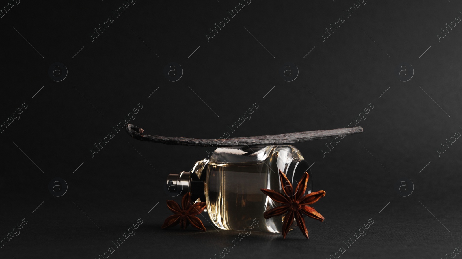 Photo of Bottle of luxurious perfume and spices on black background