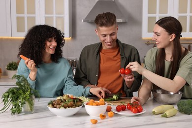 Photo of Friends cooking healthy vegetarian meal at white marble table in kitchen