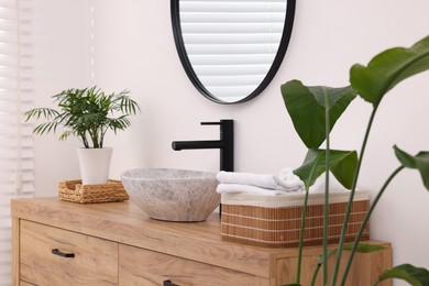 Stylish bathroom interior with mirror, vessel sink, wooden vanity and green houseplants