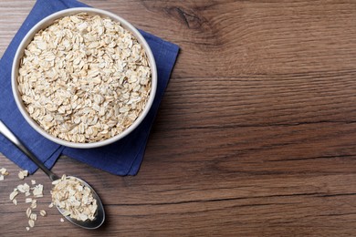 Photo of Bowl and spoon with oatmeal on wooden table, flat lay. Space for text