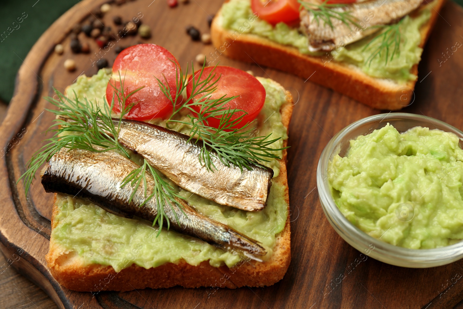 Delicious sandwich with sprats, tomato, dill and avocado puree on wooden board, closeup Photo of Delicious sandwich with sprats, tomato, dill and avocado puree on wooden board, closeup