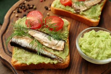 Photo of Delicious sandwich with sprats, tomato, dill and avocado puree on wooden board, closeup