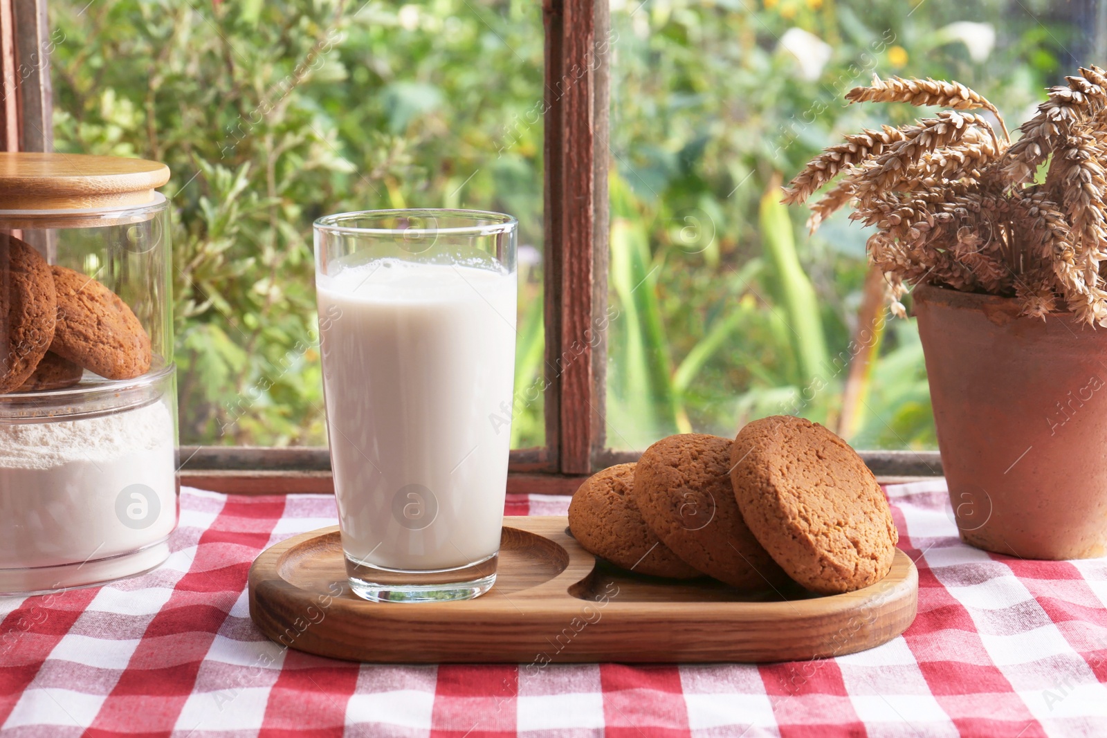 Photo of Glass of milk with cookies on red checkered tablecloth indoors