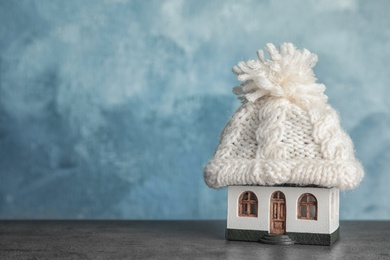 Photo of House model with knitted hat on table against color background, space for text. Heating concept