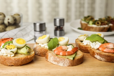 Photo of Cutting board of delicious bruschettas with shrimps on kitchen table