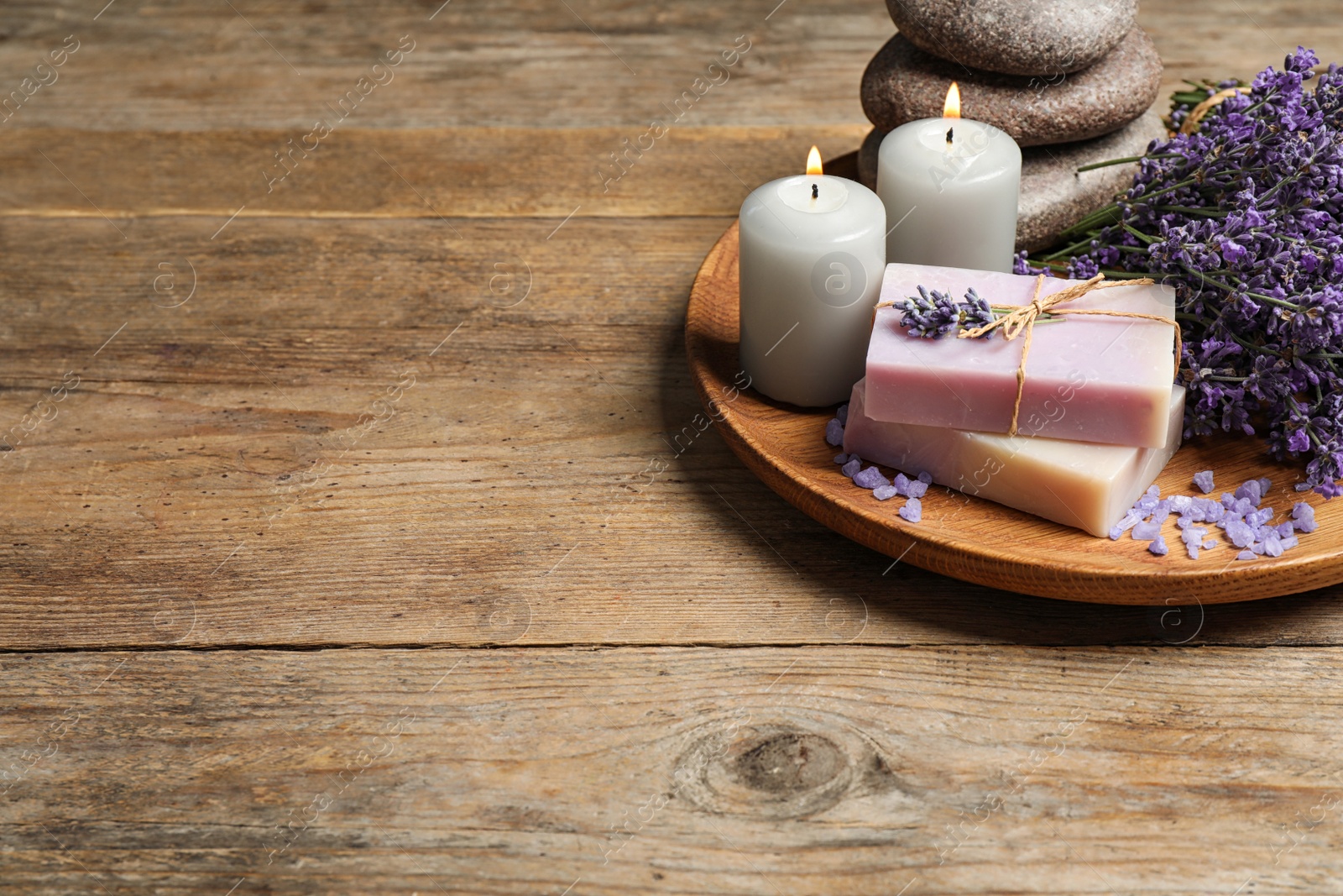 Photo of Burning candles, stones, soap bars and lavender flowers on wooden table. Space for text