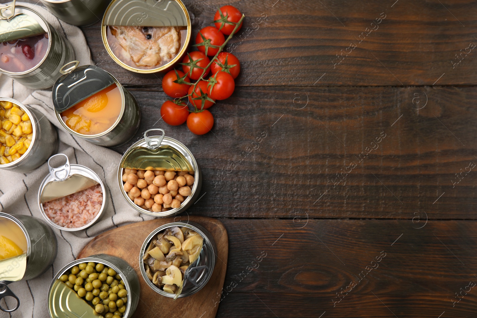 Photo of Open tin cans with different products on wooden table, flat lay. Space for text