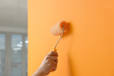 Worker using roller to paint wall with orange dye indoors, closeup