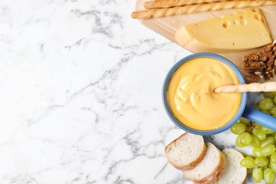 Flat lay composition with pot of delicious cheese fondue on marble table, space for text