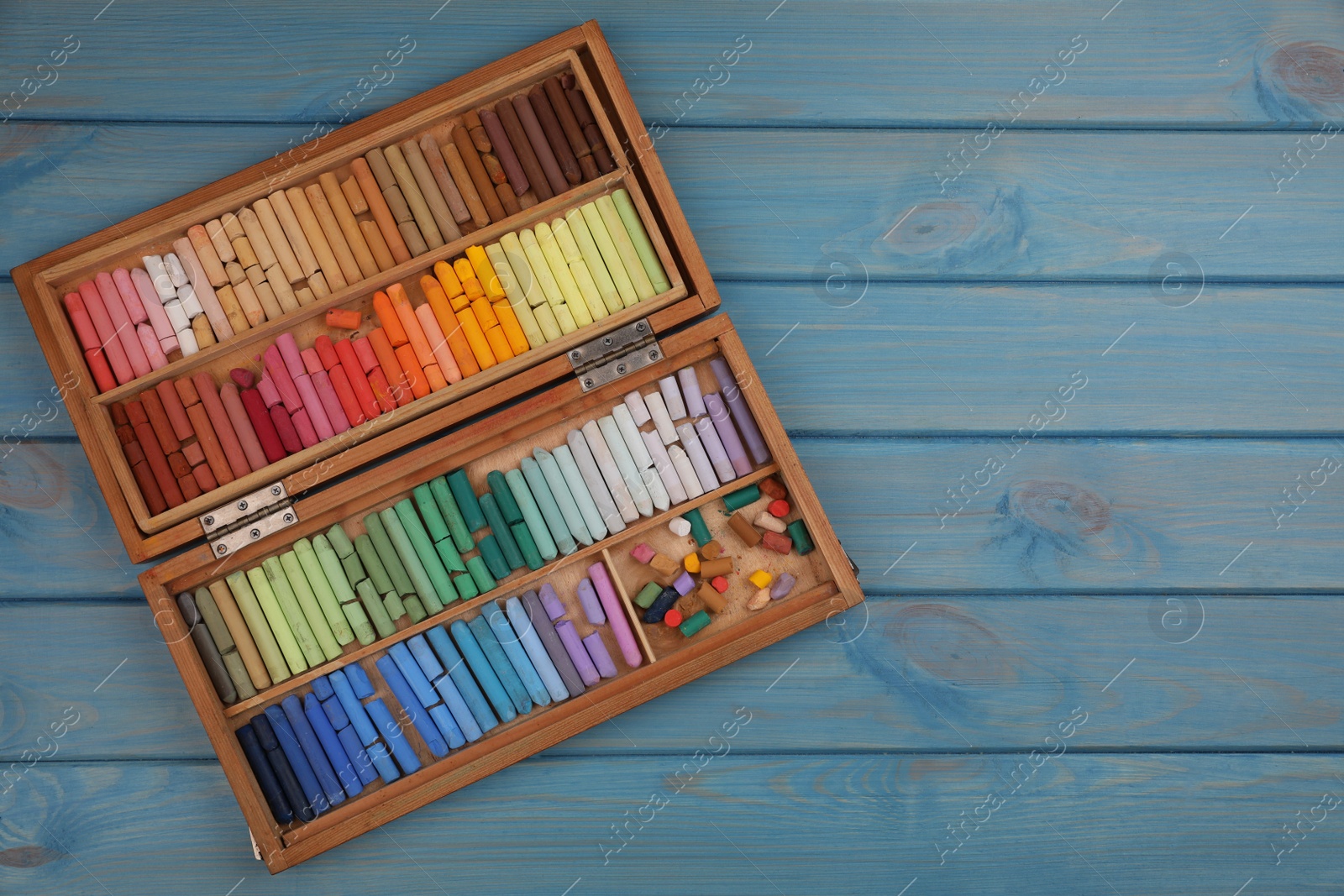 Photo of Drawing pastel set in box on light blue wooden background, top view