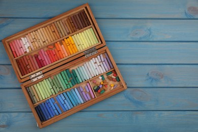 Photo of Drawing pastel set in box on light blue wooden background, top view