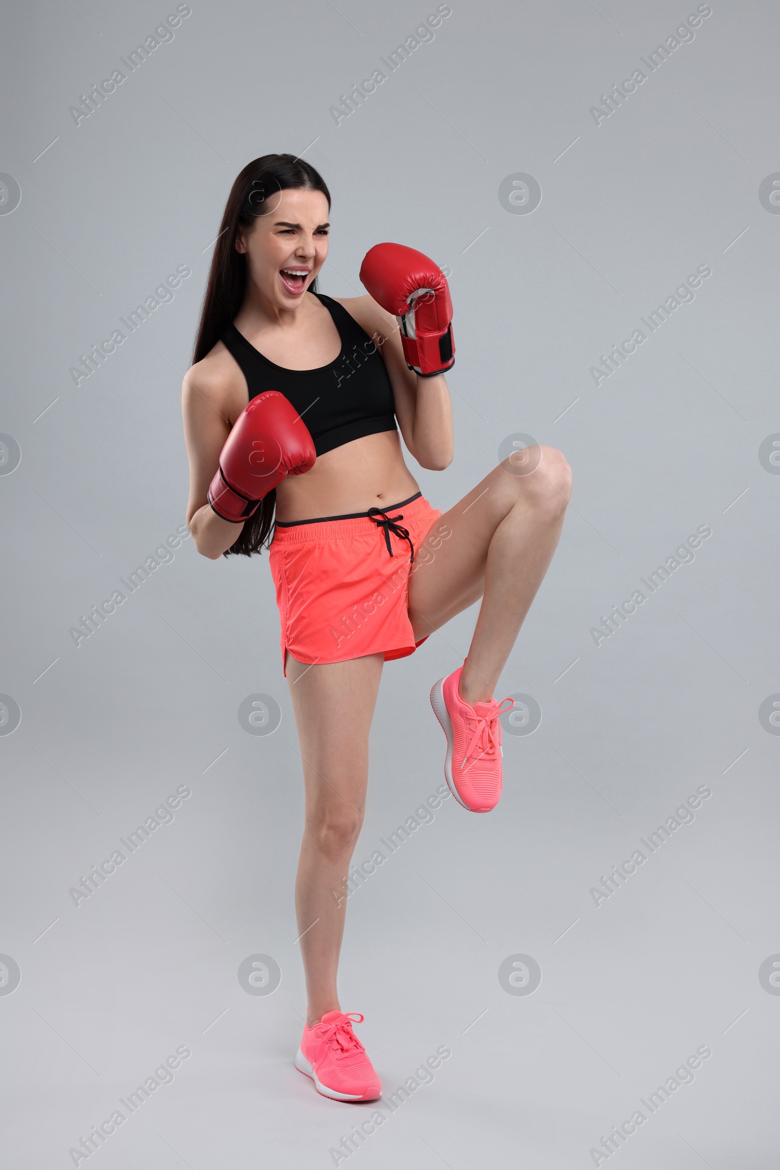 Photo of Beautiful woman in boxing gloves training on grey background