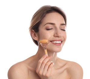 Young woman using natural jade face roller on white background