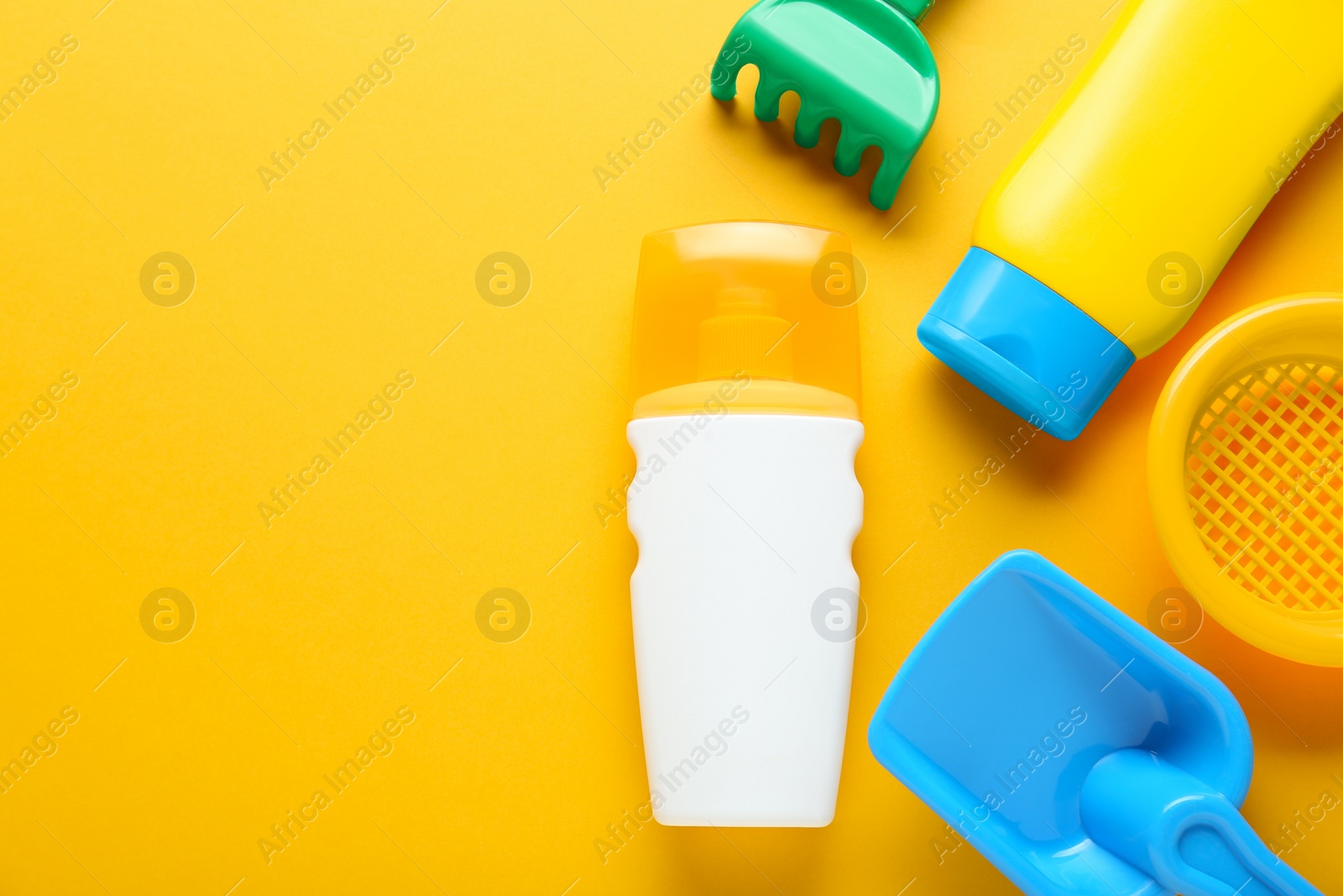 Photo of Different suntan products and plastic beach toys on orange background, flat lay. Space for text