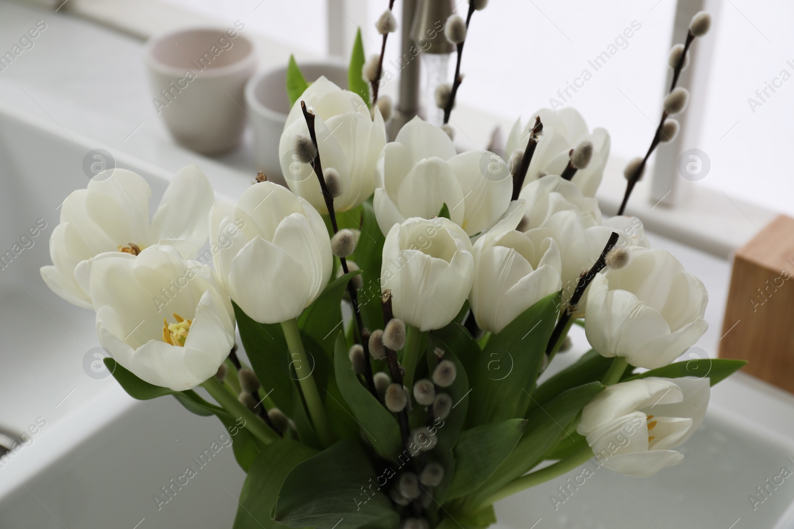 Photo of Beautiful bouquet of willow branches and tulips in kitchen sink, closeup