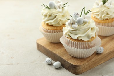 Photo of Tasty Easter cupcakes with vanilla cream and candies on gray table, closeup. Space for text