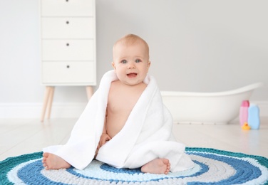 Cute little baby with soft towel on rug in bathroom