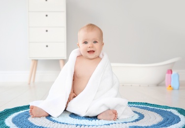 Photo of Cute little baby with soft towel on rug in bathroom