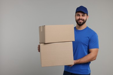 Photo of Happy young courier with parcels on grey background, space for text