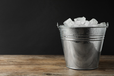 Metal bucket with ice cubes on wooden table. Space for text