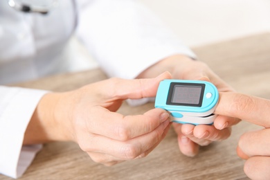 Doctor checking man's pulse with medical device in hospital, closeup