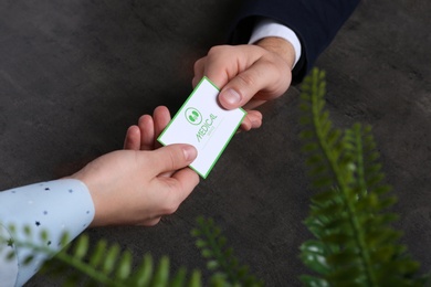 Man giving medical business card to woman on dark background, closeup. Nephrology service