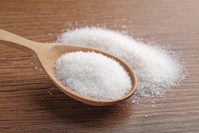 Photo of Granulated sugar and spoon on wooden table, closeup