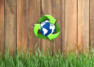 Green grass and illustration of recycling symbol with Earth on wooden fence