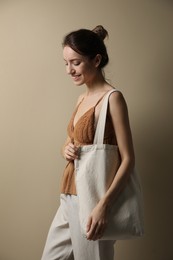 Photo of Happy young woman with blank eco friendly bag against beige background