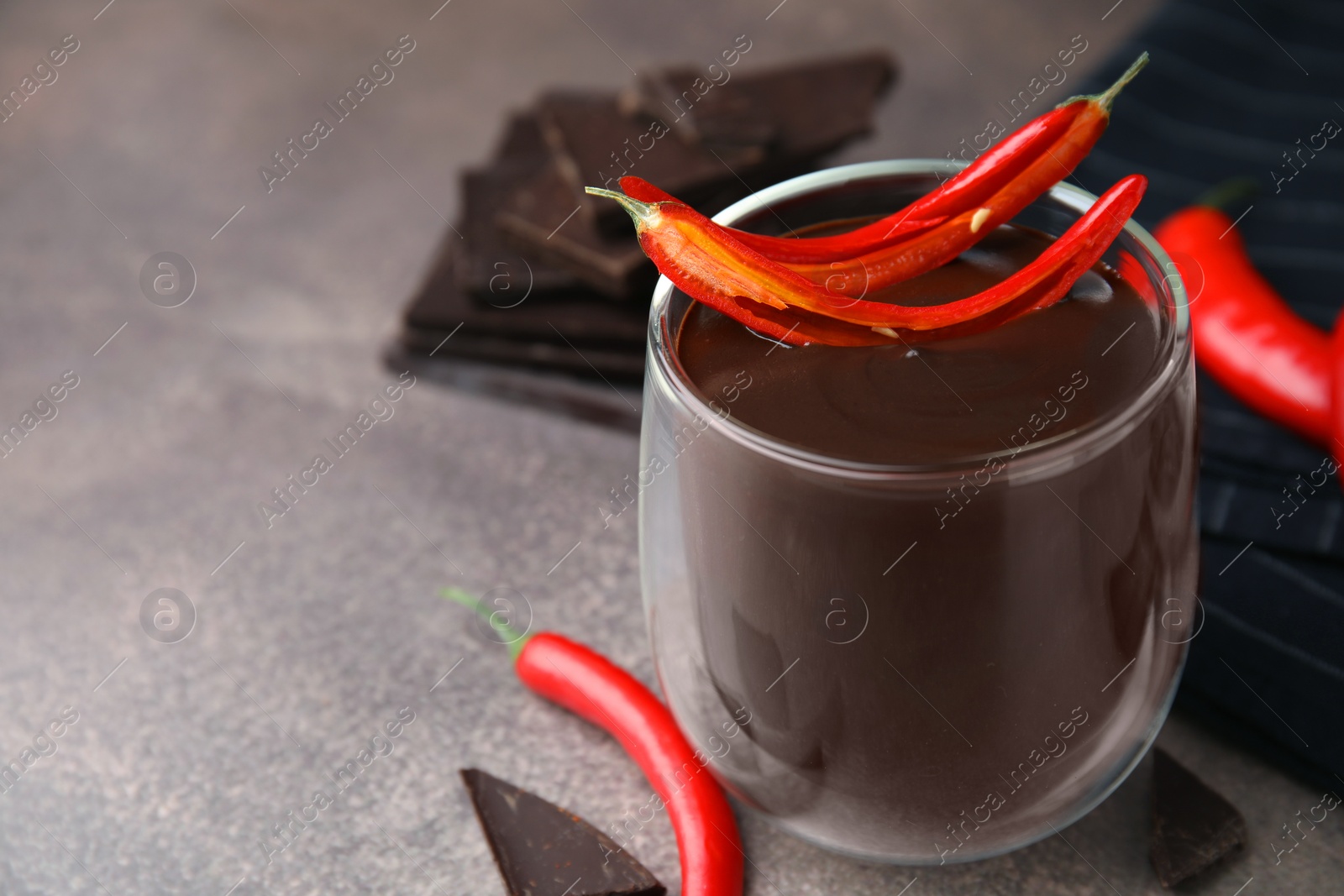 Photo of Delicious hot chocolate with chili peppers on brown textured table, closeup. Space for text