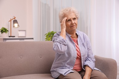 Photo of Senior woman with headache sitting on sofa at home. Space for text