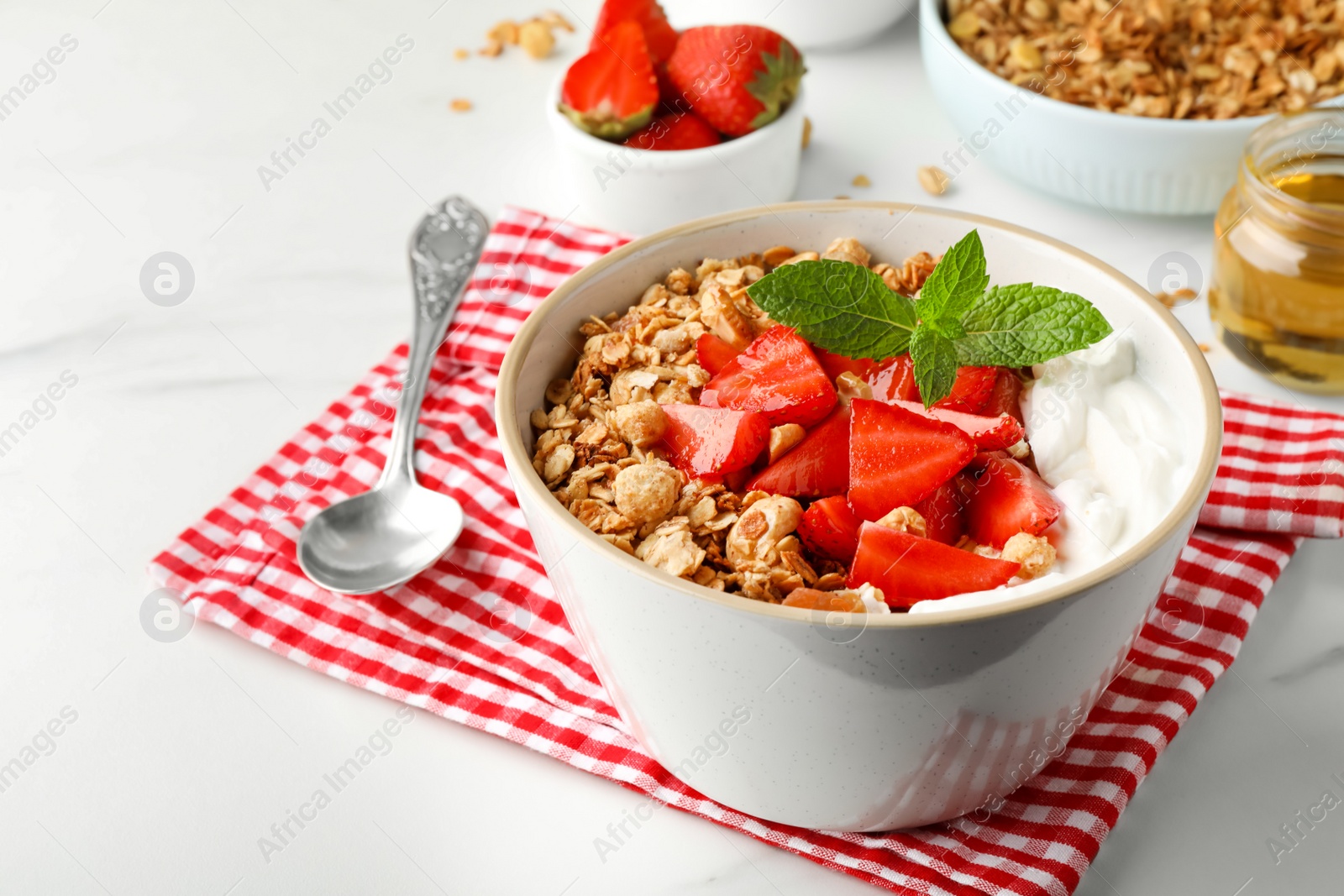 Photo of Bowl with tasty granola and strawberries served on white table. Space for text