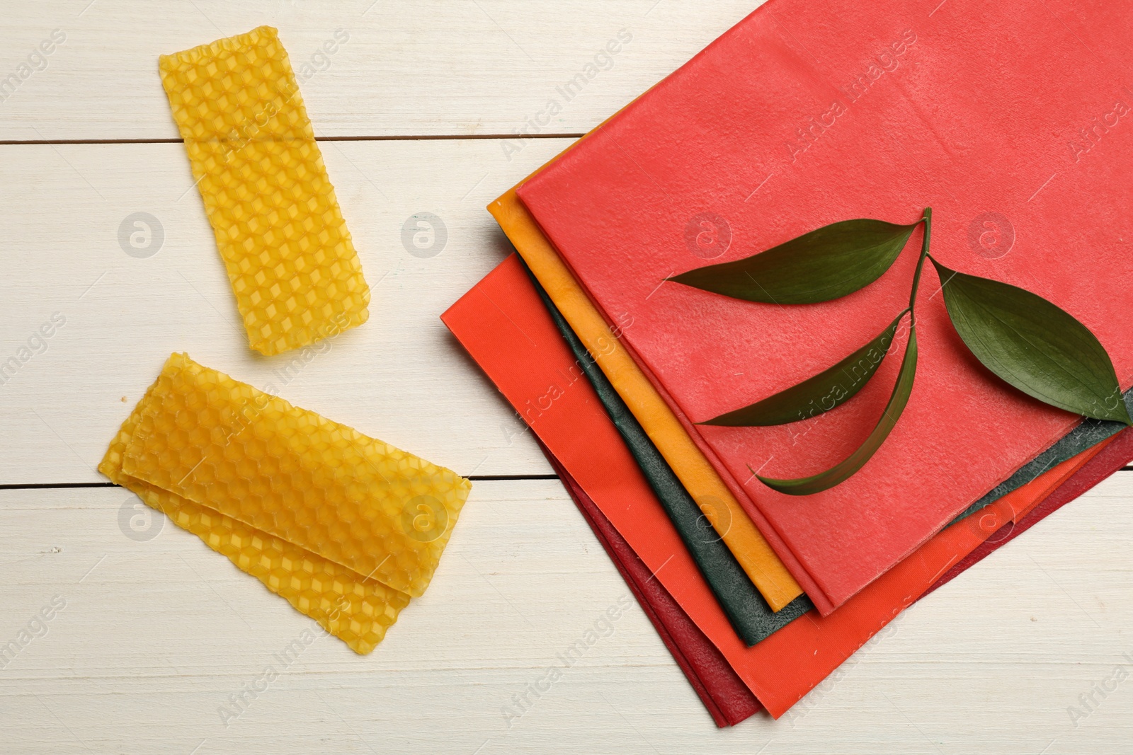 Photo of Colorful beeswax food wraps and fresh leaves on white wooden table, flat lay