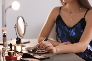 Photo of Young woman applying makeup indoors