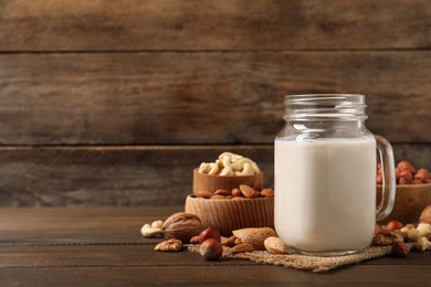 Photo of Vegan milk and different nuts on wooden table. Space for text