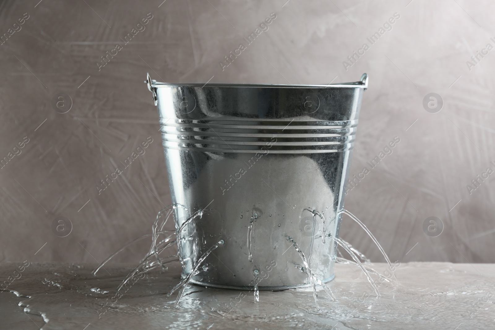 Photo of Leaky bucket with water on table against grey background
