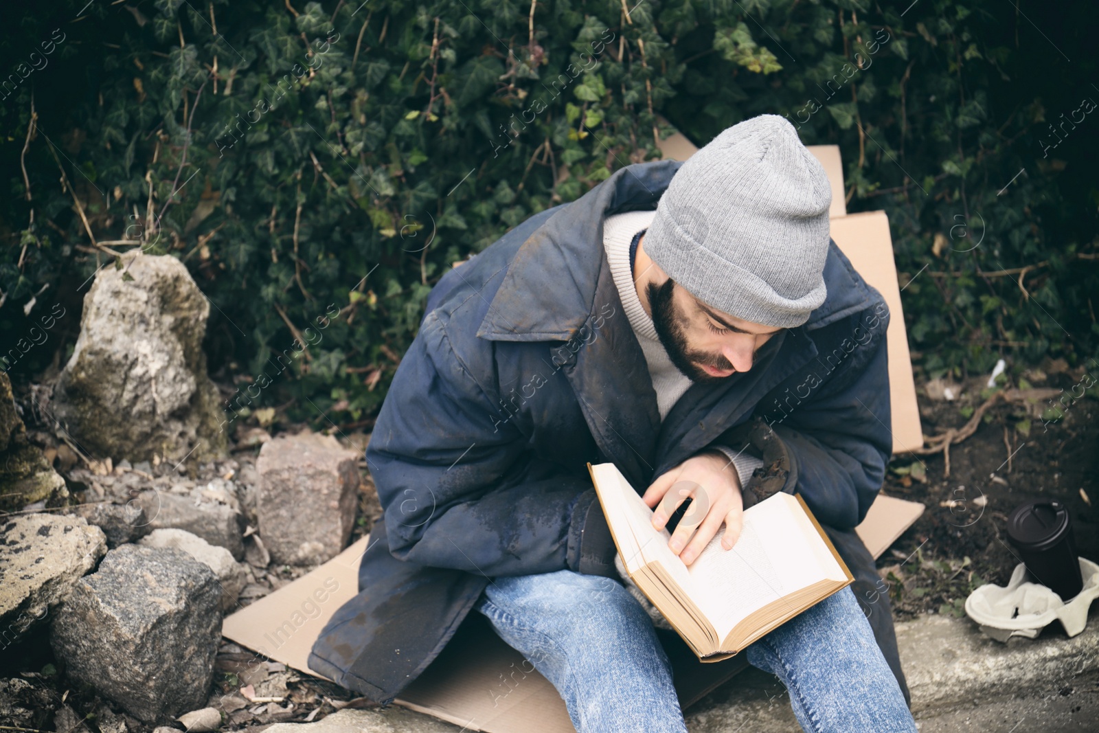 Photo of Poor homeless man with book on street in city