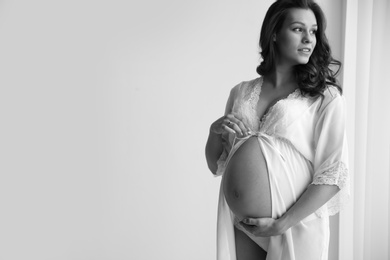 Young pregnant woman in lace nightgown on light background, black and white effect. Space for text